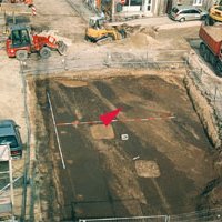 Abbildung 3: Marktplatz von Freyburg. Planum in Fläche 2. In der anstehenden, homogen dunklen Schwarzerde zeichnen sich die eingetieften mittelalterlichen Befunde deutlich ab. Stellenweise haben sich Reste des mittelalterlichen Laufhorizontes und Pflasters erhalten. Die Lage der Fibel ist gekennzeichnet. 18.04.2002. © Landesamt für Denkmalpflege und Archäologie Sachsen-Anhalt, Gert Pie.